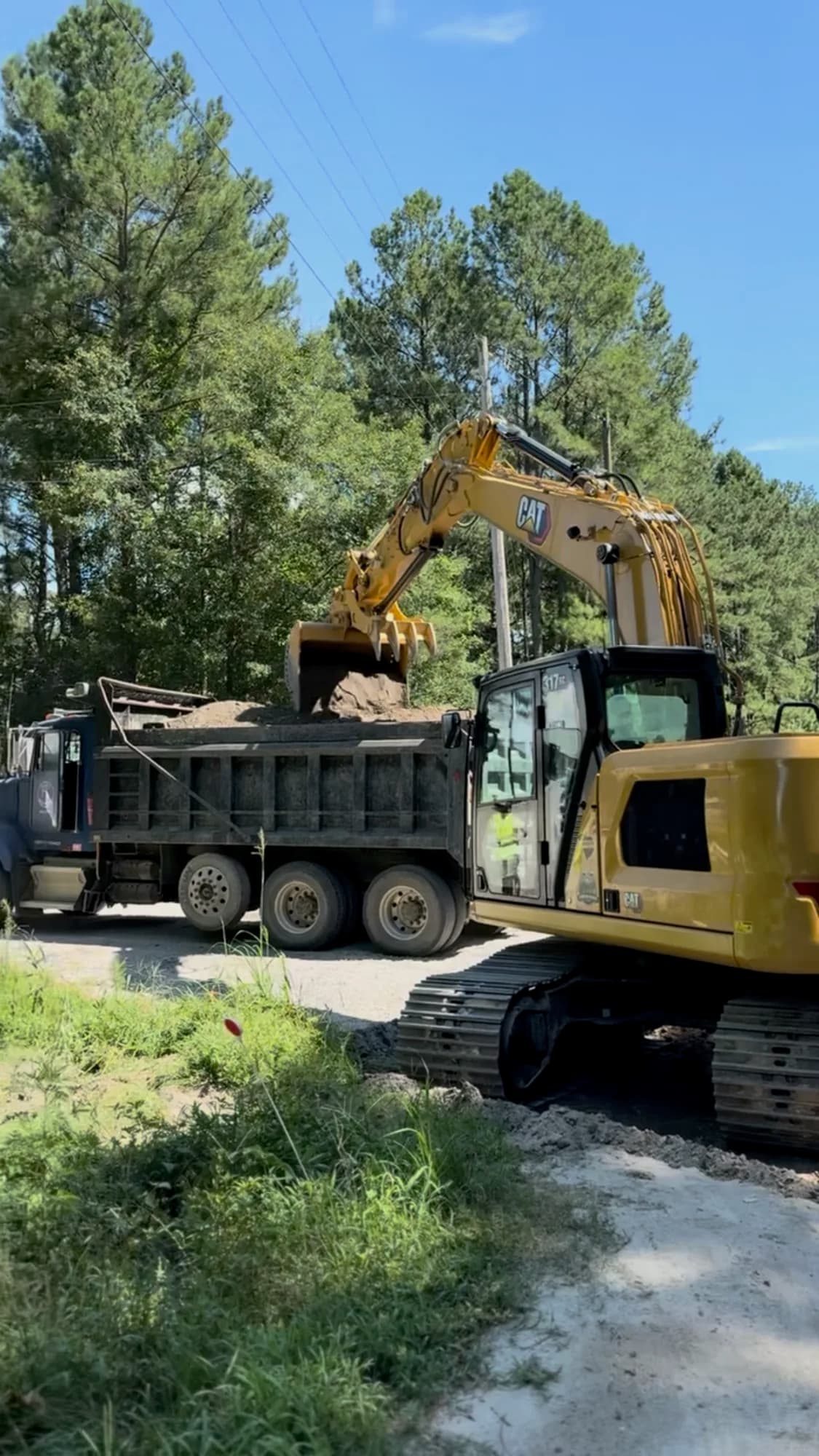 Ward Excavation CAT excavator loading spoil into a tandem dump truck on a rural Carolinas road.